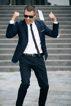 Portrait shot of cheerful rich handsome businessman in glasses and suit throws money. Happy good looking man throwing dollars. Money rain, falling dollars.