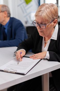 Senior businesswoman reading paperwork in conference room before signing. Executive director meeting shareholders in start up office, making satisfactorily agreement.