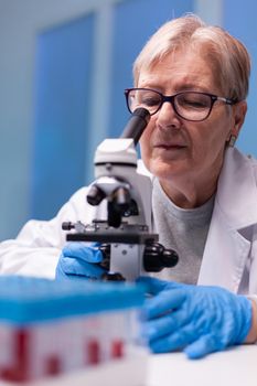 Senior chemist researcher in white coat looking in high end microscope for disease expertise. Modern laboratory for scientific research with professional equipment for virus study and diagnosis biotechnolog development