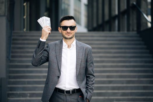 Portrait of satisfied businessman holds money. Lifestyle, richness, joy, success. Happy rich successful man holds dollars outdoors.