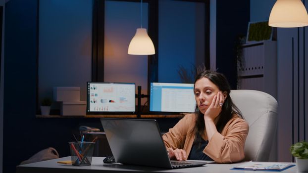 Exhausted workaholic executive manager woman typing financial strategy on laptop computer analysing economic statistics. Businesswoman working in startup company office checking report late at night