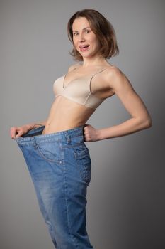 Young Woman Admiring the Result of Weight Loss While Wearing Old Jeans. Happy Female After Lost Weight. Vertical Shot