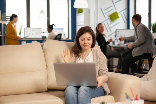 Business woman talking during video conference calling from laptop sitting on couch. Manager executive communicating in online virtual chat remote meeting, looking at pc working from modern office