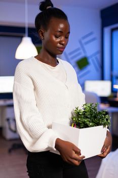 African woman worker holding office carboard fired from job with a sad, depressed expression. Unemployed packing things late at night. woman leaving workplace office in midnight.