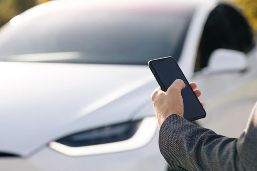 Person controls a self-driving electric car using mobile application. Autonomous autopilot driverless car. Smartphone app. Sensor scanning road ahead for vehicles, danger, speed limits