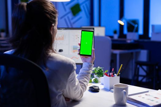 Freelancer looking at mobile phone with green screen display during online videocall meeting sitting at desk in business office. Businesswoman watching desktop monitor with green mockup, chroma key