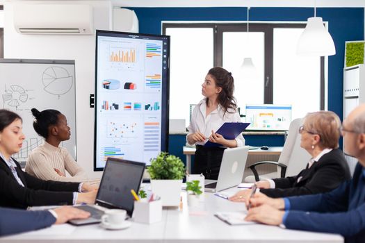 Woman executive leader coach presenter giving financial presentation in modern office boardroom for corporate employees. Multiethnical businesspeople working in professional startup financial office during conference meeting.