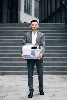Young happy businessman returns to work after vacation. New employee on first day at work carrying box with stuff to his new workplace. Concept of work career and success.
