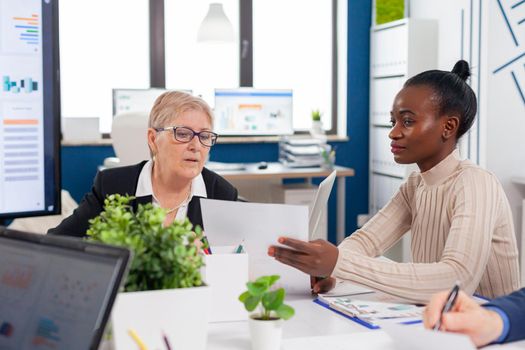 African employee in financial business board meeting room talking with senior entrepreneur investors looking analysing project documents. Personal colleagues of startup.