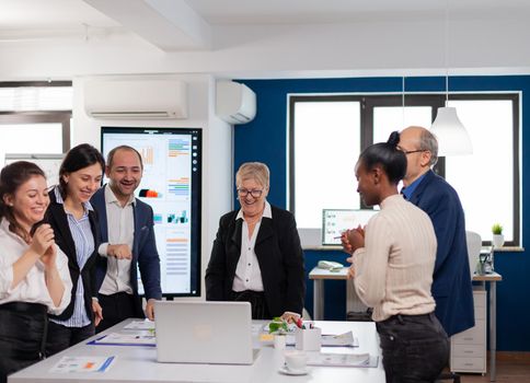 Financial corporate team overjoyed in conference room looking at laptop. Multiethnical partners coworkers celebrate successful teamwork result at company briefing