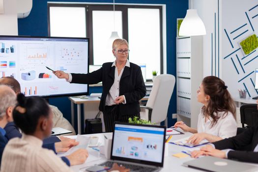 Senior startup businesswoman holding presentatin in conference room briefing, graph, information. Corporate staff discussing new business application with colleagues looking at screen