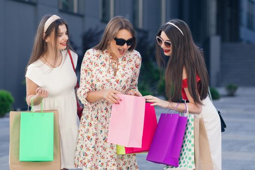 Young girls with shopping bags in the city. Girls walking around the city after shopping. Smiling women hold in hands colorful bags. Consumerism, purchases, sales.
