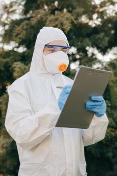 Doctor epidemiologist fighting with coronavirus COVID-19. Coronavirus Protection Pandemic Threat Covid 19. Woman in a Protective Insulating Suit and Mask notes the Data in a Notebook