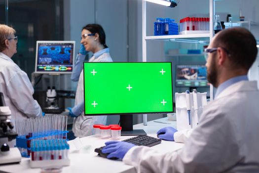 Biochemist working in laboratory using green mock-up screen for biochemistry experiment with chroma key monitor. Team of microbiologists doing vaccine analysis and discovery treatment cure against covid19