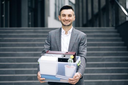 Happy businessman returns to work after vacation. New employee on first day at work carrying box with stuff to his new workplace. Concept of work career and success.