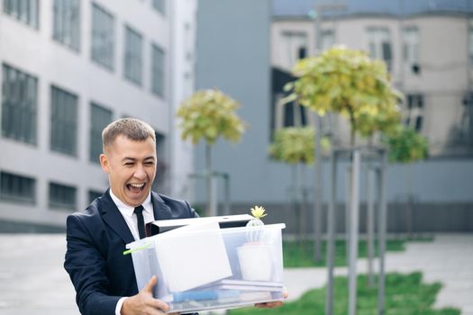 Happy businessman walking the street with box of stuff as leaving business center and dancing. Male office worker leaving job and celebrating. Fired cheerful man. Great day, good mood.
