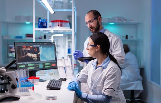 Woman scientist and man doctor studying virus expertise in medicine lab working with professional technology equipment. Multiethnic team of medical researchers working together to discovering a cure against rare disease