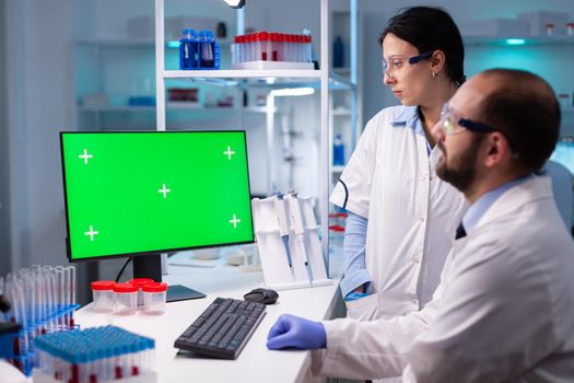 Modern medical research laboratory with two scientists using computer with green chroma key screen. Doctors specialists discussing innovative treatment against covid19 using high technology equipment.