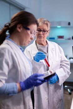 Professional scientist and senior doctor discussing resultes of blood test holding tablet equipped laboratory Specialist team of medical researchers working in sterile lab wearing protection glasses