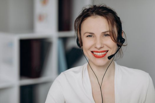 Pretty woman talking with headset in a call center looking camera. Attractive young female customer service agent talking to a customer with a telephony headset as she looks at the camera.