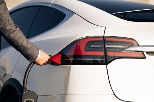 Unrecognizable businessman unplugging electric car. Luxury white electrical car full. Electrical power filling compete and cable disconnected. Save ecology alternative energy sustainable of future.