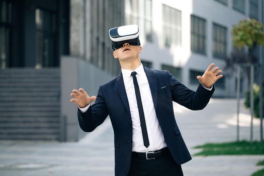 Handsome man wearing virtual reality headset. Augmented Reality. Businessman touch something using modern 3D vr glasses near office building. This new technology offers new 3D dimensions.