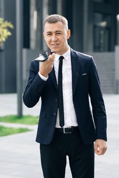 Young business man talking on phone near modern office building. Businessman use smartphone to send voice messages outdoors at downtown.