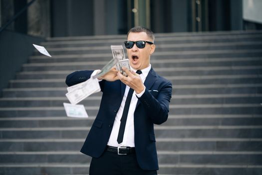 Funny man throws money. Young happy businessman scatter the dollars in the street near the office center. Money rain, falling dollars. Successful business.