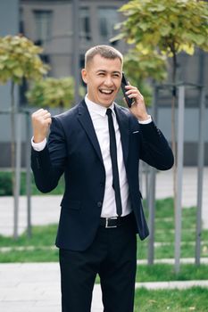 Happy person reading good news on mobile phone outdoors. Surprised man celebrating victory at remote workplace. Successful in suit boss company confident. Vertical screen orientation