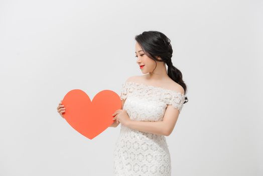 Attractive young Asian woman holding red love shape and standing over white background.