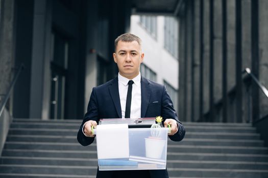 Portrait sad male office worker in depression with box of personal stuff. Businessman lost job. Fired man outdoors. Depressed jobless person. Unemployment concept. Left without money.