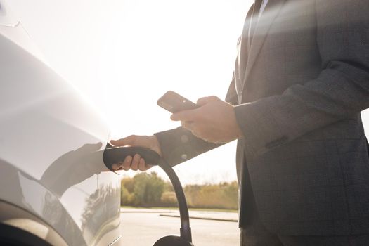 Businessman unplugging electric car from charging station. Luxury white electrical car full. Disconnecting the cable when electrical power filling compete