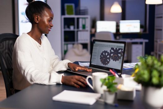 African mechanical designer working on computer late at night doing overtime to finish project. Freelancer studying prototype idea on pc showing cad software on device display.