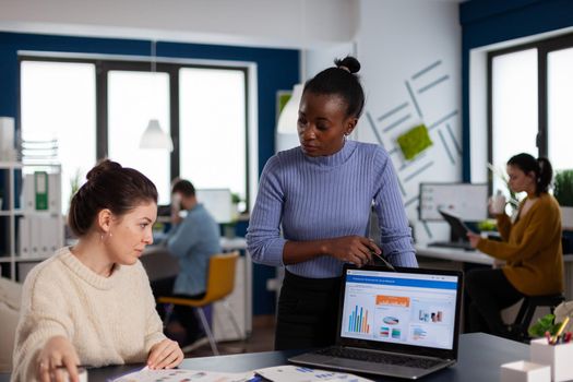 Marketing statistics analysed by diverse team colleagues of start up company. Multiethnic employees gathered in co-working space discussing financial charts.