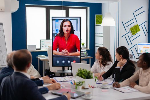 Diverse executive team meeting at conference video call looking at huge display. Business people talking to webcam, do online conference participate internet brainstorming, distance office discussion