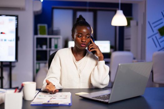 African businesswoman discussing with partner late at night from office. Busy focused freelancer doing overtime for job reading writing, searching, respecting deadline of financial project, overworking.
