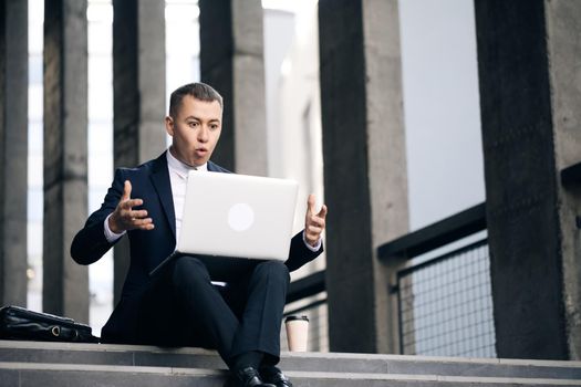 Angry business man boss in suit having video call on laptop computer at street. Serious business man using computer outdoors. Furious male freelancer or boss working on computer.