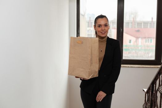 Businesswoman climbing stairs in startup company office hoding takeaway food meal bag during takeout lunchtime. Delivery guy delivering fastfood lunch order package to manager client