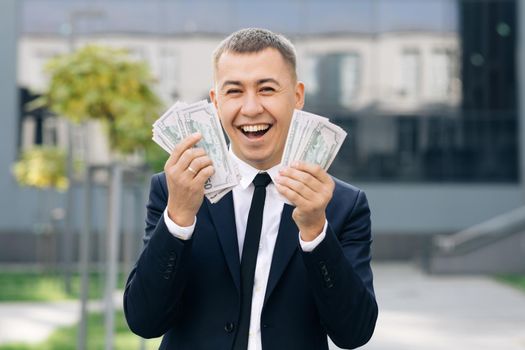 Happy excited businessman with money - U.S. currency dollars banknotes. Symbol of success, gain, victory. Man shows money and celebrating.