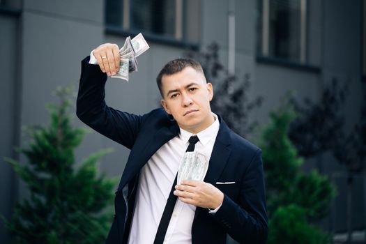 Man shows money and celebrating success, victory while looking to camera. Outdoors. Amazed happy excited businessman with money - U.S. currency dollars banknotes.