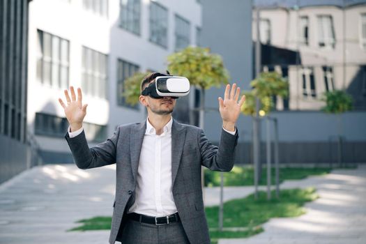Augmented Reality. Businessman touch something using modern 3D vr glasses near office building. This new technology offers new 3D dimensions. Handsome man wearing virtual reality headset.