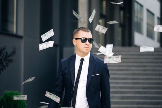 Money rain, falling dollars. Portrait shot of cheerful rich handsome businessman in glasses and suit throws money. Happy good looking man throwing dollars.