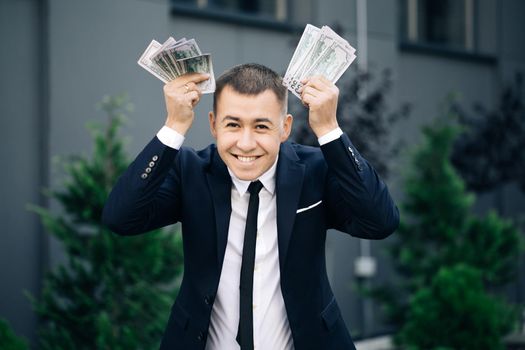 Man shows money and celebrating success while looking to camera. Amazed happy excited businessman with money - U.S. currency dollars banknotes.