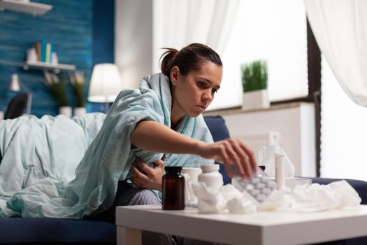 Young sick adult taking medicine for flu at home to treat disease infection sickness. Caucasian woman ill with seasonal covid 19 symptoms treating cold sore throat and nose