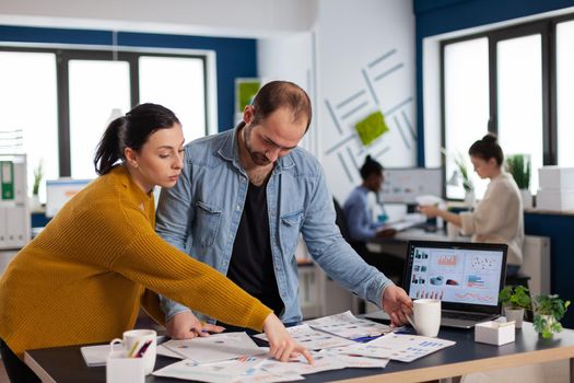 Businessman and cowokers in startup office checking charts, discussing strategy collaboration. Diverse team of business people analyzing company financial reports from computer.