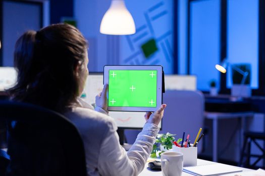 Manager woman holding tablet with green screen monitor during online web conference. Entrepreneur looking at desktop monitor display with green mockup, chroma key sitting at desk in business office