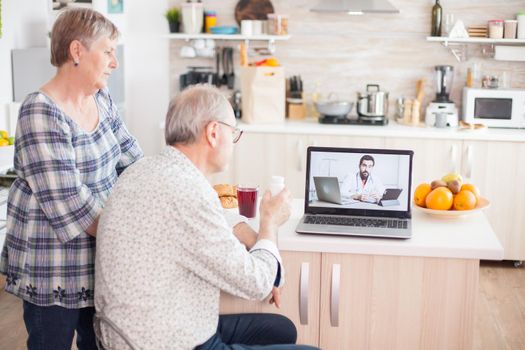 Video conference with doctor using laptop in kitchen. Online health consultation for elderly people drugs ilness advice on symptoms, physician telemedicine webcam. Medical care internet chat