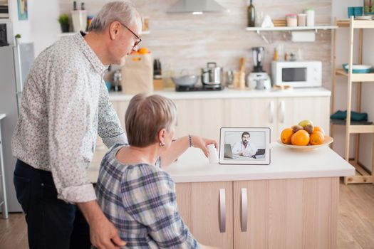 Senior woman showing pills bottle to doctor via online video call. Video conference with doctor using laptop in kitchen. Online health consultation for elderly people drugs ilness advice on symptoms, physician telemedicine webcam. Medical care internet chat