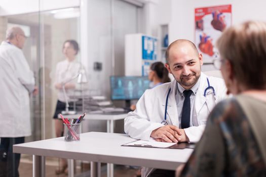 Doctor with senior patient during medical examination on hospital office wearing white coat and stethoscope. Mature medic discussing diagnosis with young sick woman on clinic corridor