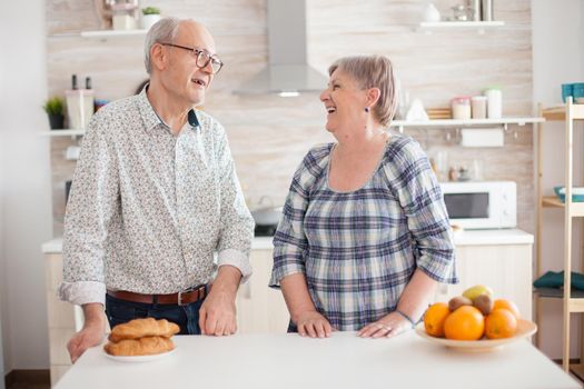 Portrait of senior couple in kitchen smiling at each other and looking at camera. Cheerful wife and husband.